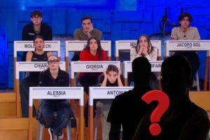 Ragazzi nei banchi scuola di Amici, due sagome nere, punto di domanda