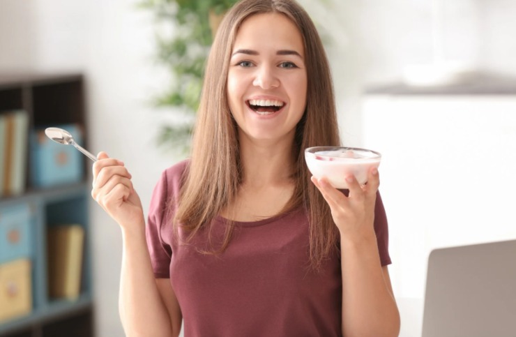 donna che mangia uno yogurt con in mano una coppetta e un cucchiaino